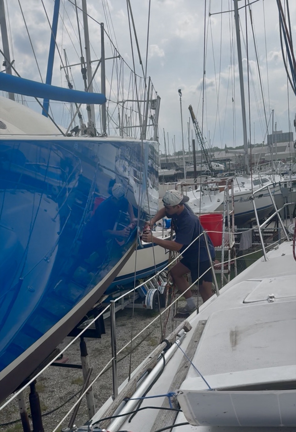 Crew member polishing the hull of a blue-hulled sailboat