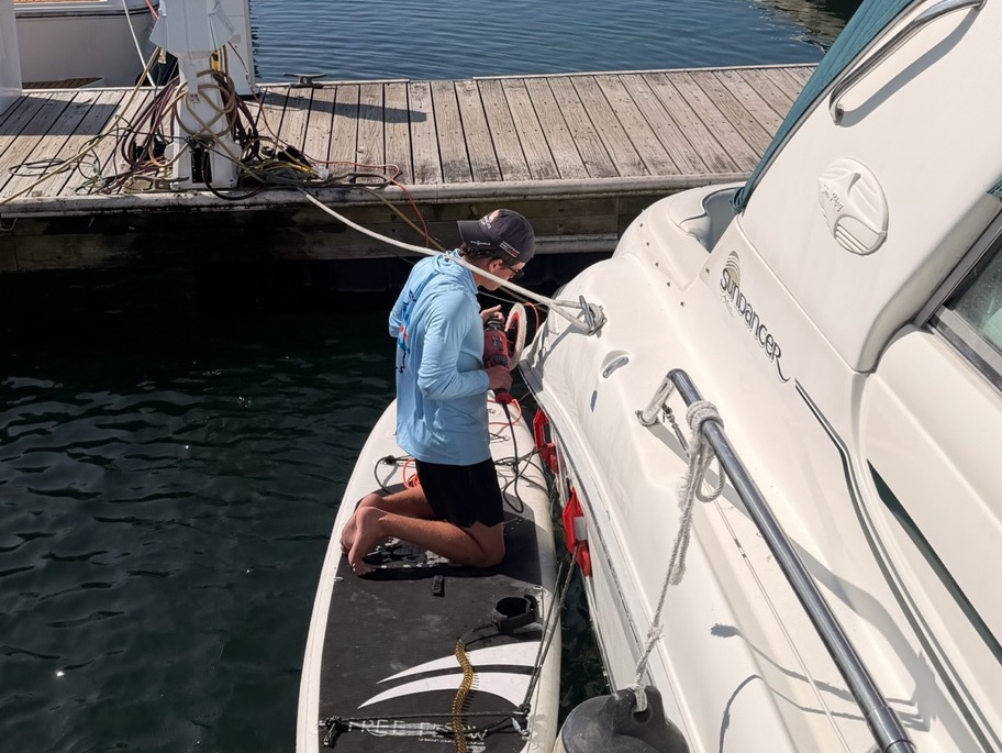 Crew member machine-buffing a boat's topsides above the rubrail