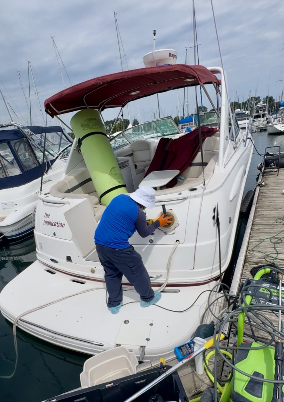 Crew member machine-buffing the transom of a cruiser named The Implication