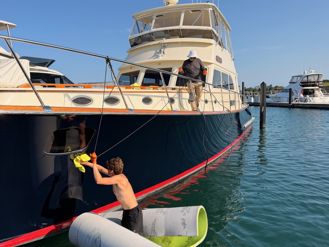 Crew member hand-detailing a boat's hull to a glossy shine